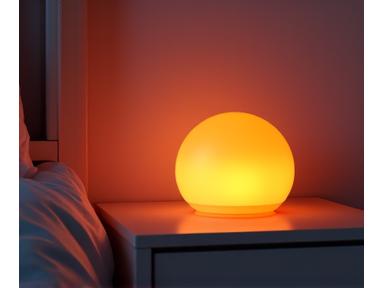 Dispositivo de luz terapéutica emitiendo una suave luz ambarina en una mesita de noche.